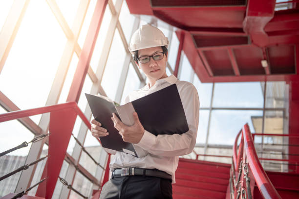istock Young Asian male engineer or architect holding files wearing protective safety helmet on red stair at construction site. Civil engineering, Architecture and building construction concept 1006696224