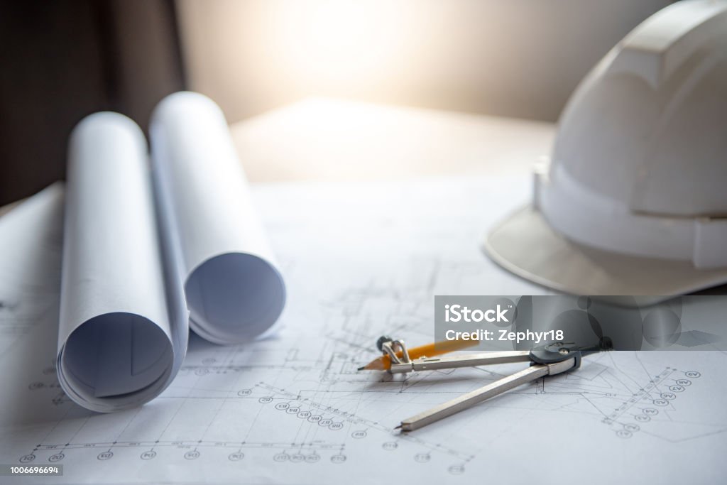 Compass tool and safety helmet on architectural drawing plan of house project, blueprint rolls on working table, Architecture and building construction industry concepts Architect Stock Photo