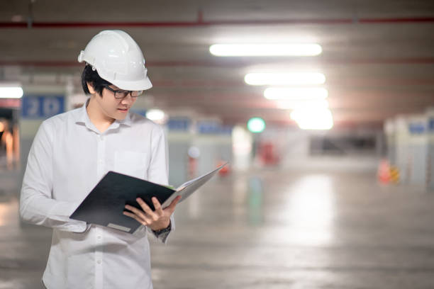 istock Young Asian male engineer or architect holding files wearing protective safety helmet on red stair at construction site. Civil engineering, Architecture and building construction concept 1006696736