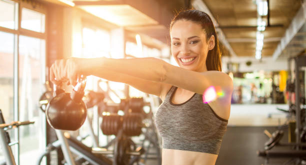giovane donna in forma che si allena con la campana del bollitore in palestra - picking up weight women sport foto e immagini stock