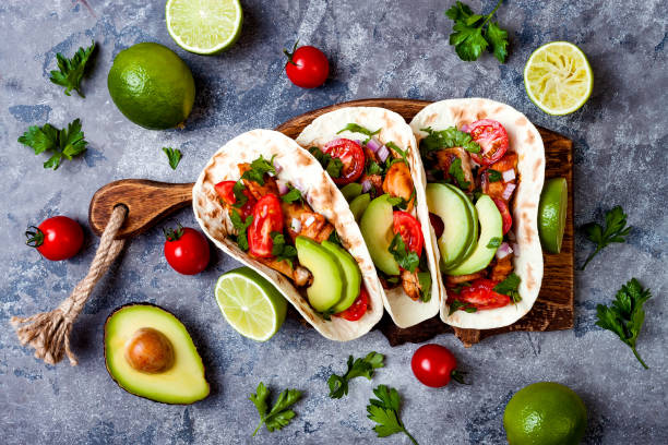 istock Mexican grilled chicken tacos with avocado, tomato, onion on rustic stone table. Recipe for Cinco de Mayo party. Top view, overhead, flat lay. 1006733506