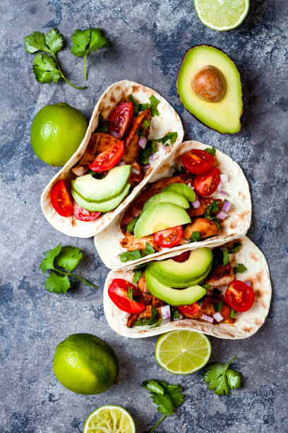istock Mexican grilled chicken tacos with avocado, tomato, onion on rustic stone table. Recipe for Cinco de Mayo party. Top view, overhead, flat lay. 1006733526