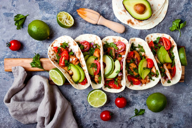 istock Mexican grilled chicken tacos with avocado, tomato, onion on rustic stone table. Recipe for Cinco de Mayo party. Top view, overhead, flat lay. 1006733572