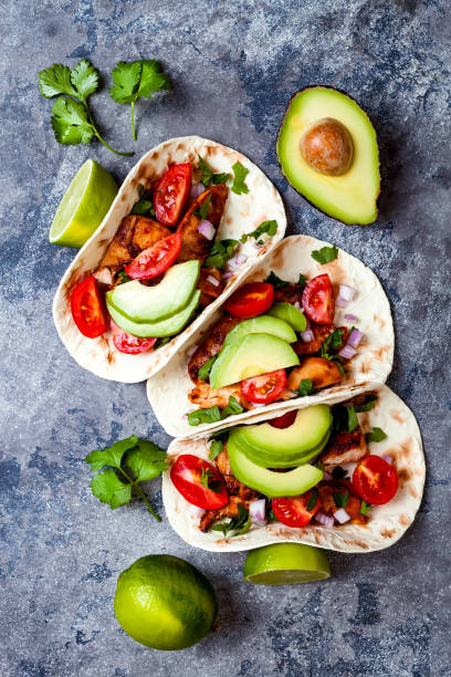 istock Mexican grilled chicken tacos with avocado, tomato, onion on rustic stone table. Recipe for Cinco de Mayo party. Top view, overhead, flat lay. 1006734072