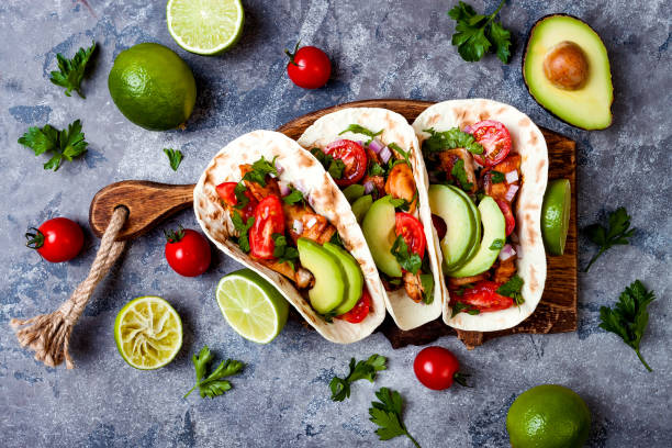 istock Mexican grilled chicken tacos with avocado, tomato, onion on rustic stone table. Recipe for Cinco de Mayo party. Top view, overhead, flat lay. 1006734092