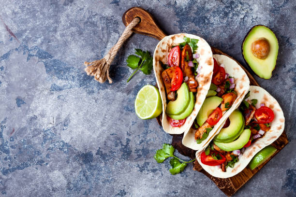 istock Mexican grilled chicken tacos with avocado, tomato, onion on rustic stone table. Recipe for Cinco de Mayo party. Top view, overhead, flat lay. 1006734170