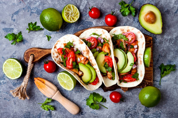 istock Mexican grilled chicken tacos with avocado, tomato, onion on rustic stone table. Recipe for Cinco de Mayo party. Top view, overhead, flat lay. 1006734186