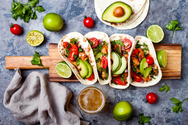 istock Mexican grilled chicken tacos with avocado, tomato, onion on rustic stone table. Recipe for Cinco de Mayo party. Top view, overhead, flat lay. 1006734198