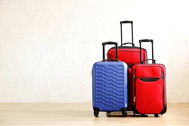 Three suitcases of different size, big & small, red textile and blue hard shell luggage with extended telescopic handle. Family trip concept. Copy space, white wall background. Fully packed baggage.