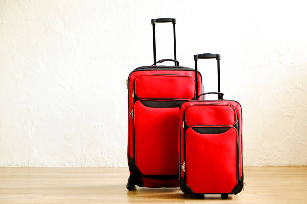 istock Two colorful red suitcases of same kind different size with telescopic handle up on wooden floor, white wall background. Family trip concept. Packed traveling luggage ready to go. Close up, copy space 1006738186