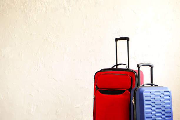 istock Red textile suitcase & blue hard shell luggage, extended telescopic handle up, white decorative texture wall background. Couples retreat trip concept. Packed traveling baggages. Close up, copy space. 1006738320