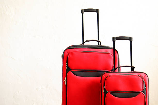 istock Two colorful red suitcases of same kind different size with telescopic handle up on wooden floor, white wall background. Family trip concept. Packed traveling luggage ready to go. Close up, copy space 1006738322