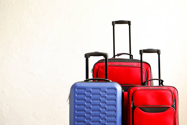 istock Three suitcases of different size, big & small, red textile and blue hard shell luggage with extended telescopic handle. Family trip concept. Copy space, white wall background. Fully packed baggage. 1006738330