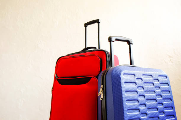 istock Red textile suitcase & blue hard shell luggage, extended telescopic handle up, white decorative texture wall background. Couples retreat trip concept. Packed traveling baggages. Close up, copy space. 1006738428