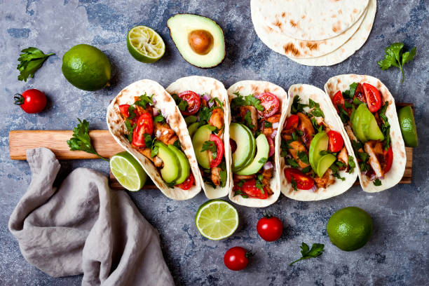 istock Mexican grilled chicken tacos with avocado, tomato, onion on rustic stone table. Recipe for Cinco de Mayo party. Top view, overhead, flat lay. 1006738530