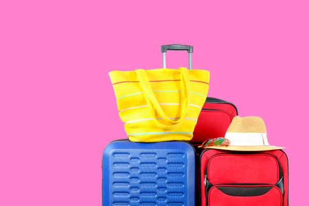istock Three suitcases, red textile & blue hard shell luggage, extended telescopic handle, straw hat, beach bag, mirrored sunglasses, pink wall background. Family trip concept. Close up, copy space 1006742072