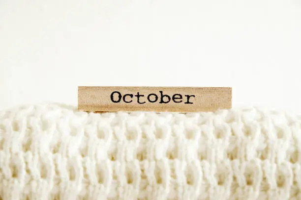 Photo of Minimalistic rustic composition with stacked vintage knitted sweaters and wooden calendar on white wall background.