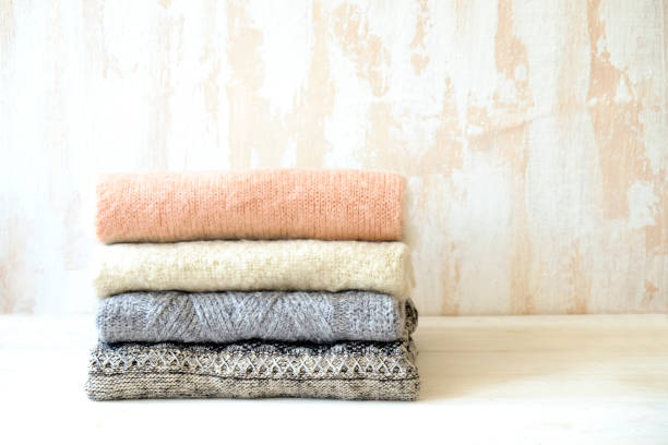 istock Minimalistic rustic composition with stacked vintage knitted sweaters on white wall background. 1006755472