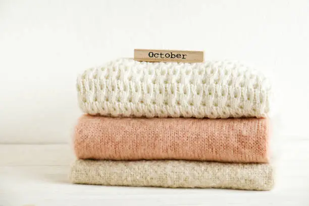 Photo of Minimalistic rustic composition with stacked vintage knitted sweaters and wooden calendar on white wall background.
