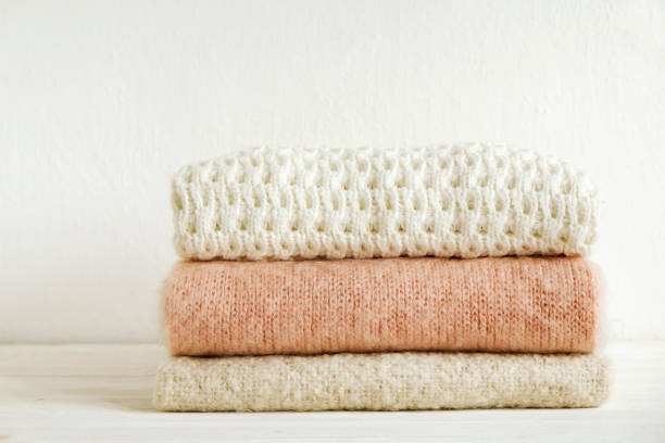 istock Minimalistic rustic composition with stacked vintage knitted sweaters on white wall background. 1006755514