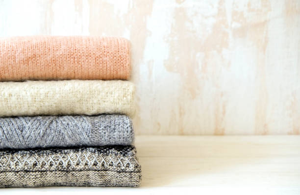 istock Minimalistic rustic composition with stacked vintage knitted sweaters on white wall background. 1006755648