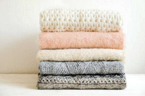 istock Minimalistic rustic composition with stacked vintage knitted sweaters on white wall background. 1006755704