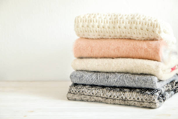 istock Minimalistic rustic composition with stacked vintage knitted sweaters on white wall background. 1006755762