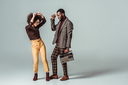 smiling african american retro styled couple dancing with vintage radio on grey