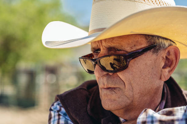 Close up portrait of senior cowboy looking away making a face over sun glasses on tip of his nose. Ranch outside Salt Lake City, Utah.