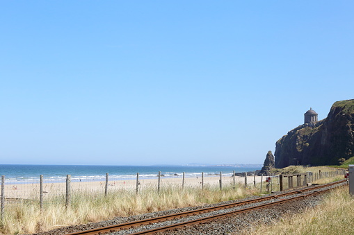 Coastal railway by the beautiful beach and North Atlantic coast of Northern Island with the Mussenden Temple perched precariously on nearby cliffs.