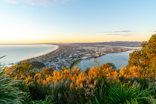 Glow of sunrise over sea and across town and harbor below and slopes of Mount Maunganui