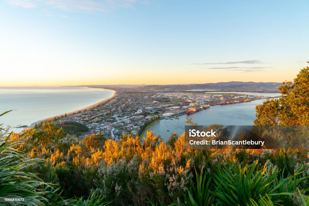 Glow of sunrise over sea and across town below and slopes of Mount Maunganui Glow of sunrise over sea and across town and harbor below and slopes of Mount Maunganui Tauranga Stock Photo
