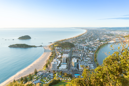 Mount Maunganui stretches south out below as sun rises on horizon and falls across ocean beach and buildings below