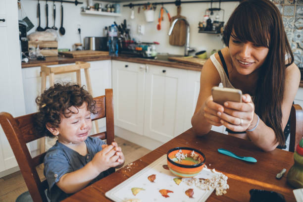 Toddler crying after making mess Toddler crying after making mess with his food while mother use smart phone boys bowl haircut stock pictures, royalty-free photos & images