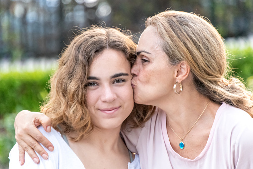 Smiling hispanic Mature mother kissing her young daughter