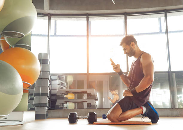 Fitness instructor using mobile phone in health club with dumbbell stock photo