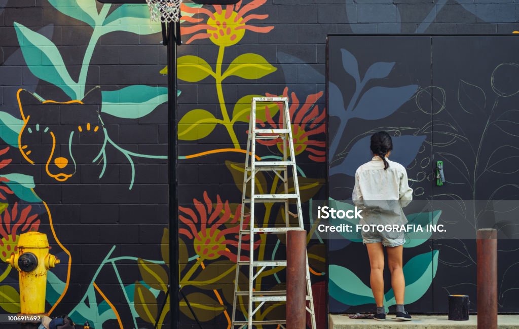 Mural artist at work Young Asian woman, mural artist creating wall art at the urban setting. Mural Stock Photo