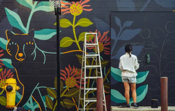 Young Asian woman, mural artist creating wall art at the urban setting.