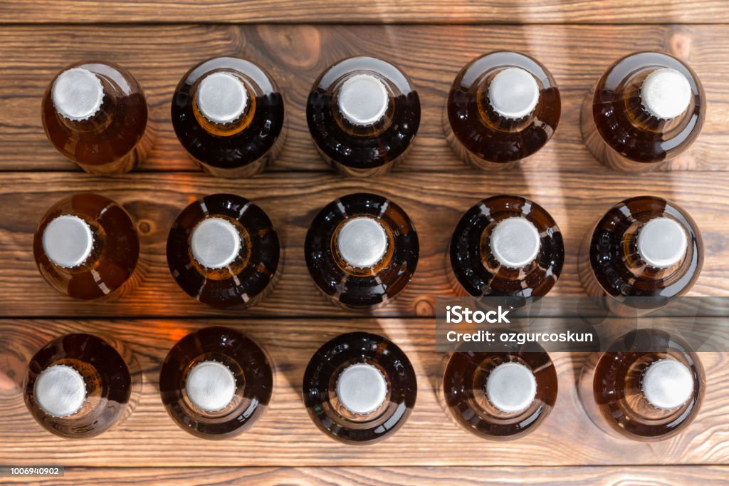 Neatly aligned rows of bottled craft beer 15 neatly aligned rows of bottled craft beer capped with bottle tops viewed top down on a wooden table Bottle Stock Photo