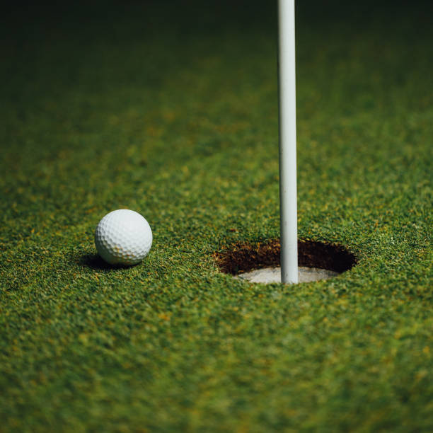 golf ball nearby hole with pin flag, green grass background golf ball nearby hole with pin flag, green grass background, close-up view night golf stock pictures, royalty-free photos & images