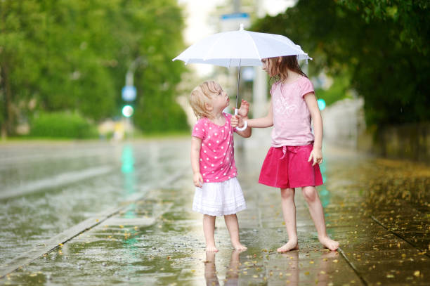 dos lindas hermanitas divirtiéndose bajo una lluvia - child dancing preschooler outdoors fotografías e imágenes de stock