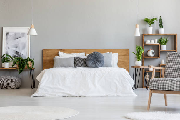 istock Patterned armchair in grey bedroom interior with poster on table with plants next to bed. Real photo 1006968286