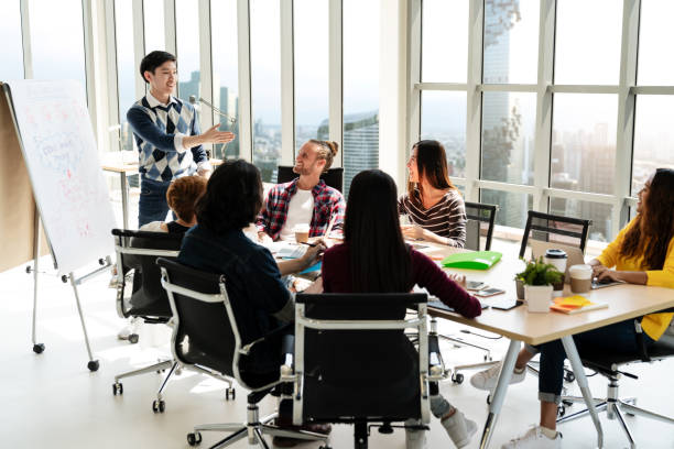 istock Young asian creative businessman standing and making presentation at modern office happy talking and brainstorming with team. Casual people business meeting concept. 1006991590