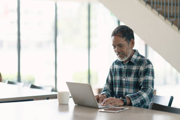istock Smiling attractive mature man with white, grey stylish short beard using smartphone gadget serving internet in modern office,co-working space or coffee shop. Old man using social network technology. 1006996296