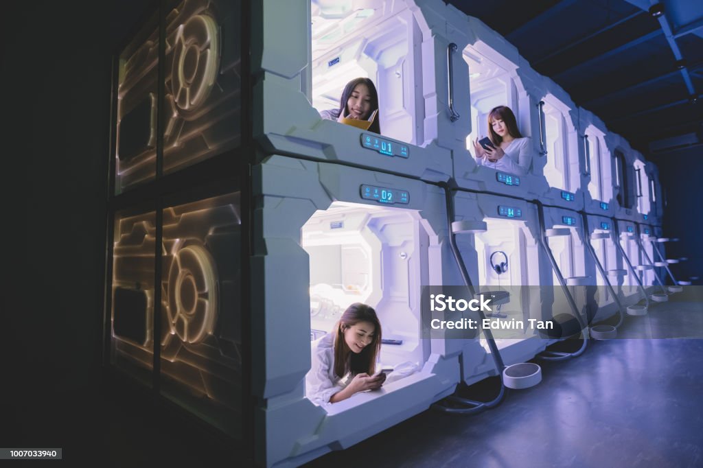 three asian chinese female tourist check in capsule hotel room and surfing internet and selfie on their bed with their mobile phone while one of them reading from her notebook Capsule Hotel Stock Photo