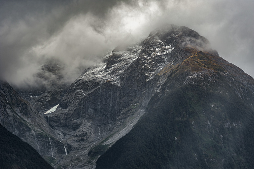 Misty clouds float above snowy mountain top with streams of water cascading at Milford Sounds, New Zealand.