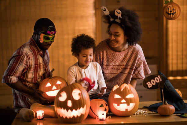 Happy African American family enjoying in Halloween at home. Happy black parents and their little son decorating their home with Jack O' Lanterns on Halloween. halloween pumpkin decorations stock pictures, royalty-free photos & images