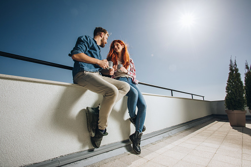Low angle view of young couple communicating on a terrace while drinking coffee.