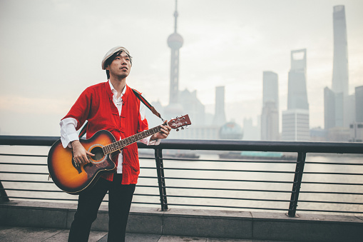 One man, standing on the street by the river, playing acoustic guitar.