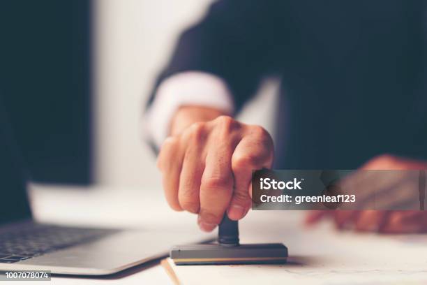 Closeup Of A Persons Hand Stamping With Approved Stamp On Document At Desk Stock Photo - Download Image Now